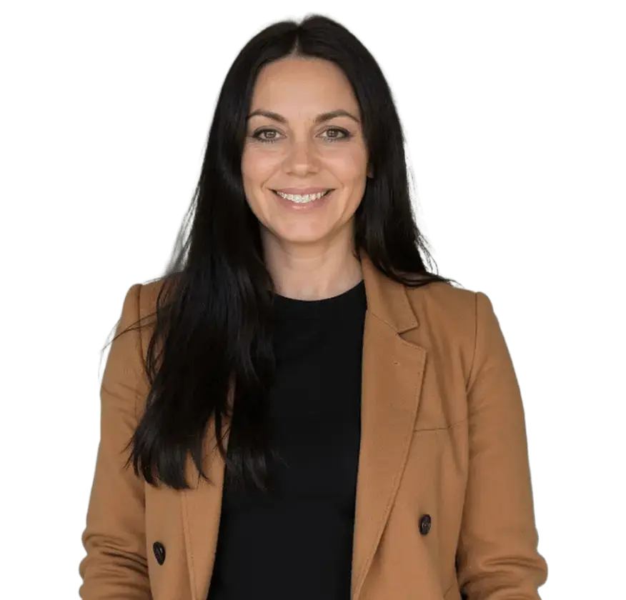 A woman with long black hair wearing a brown jacket stands confidently, showcasing her style and poise.