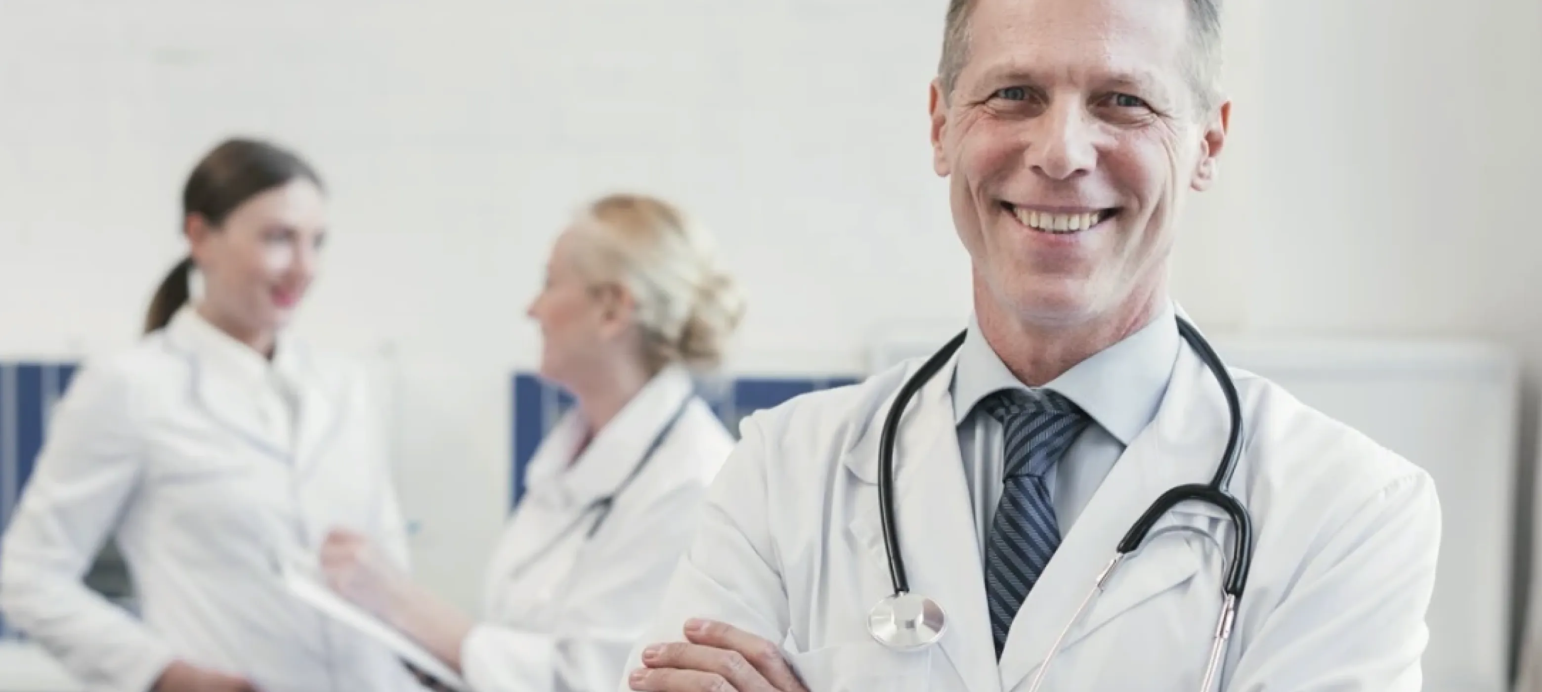 A smiling male doctor stands confidently in front of a diverse group of people, showcasing a welcoming atmosphere.