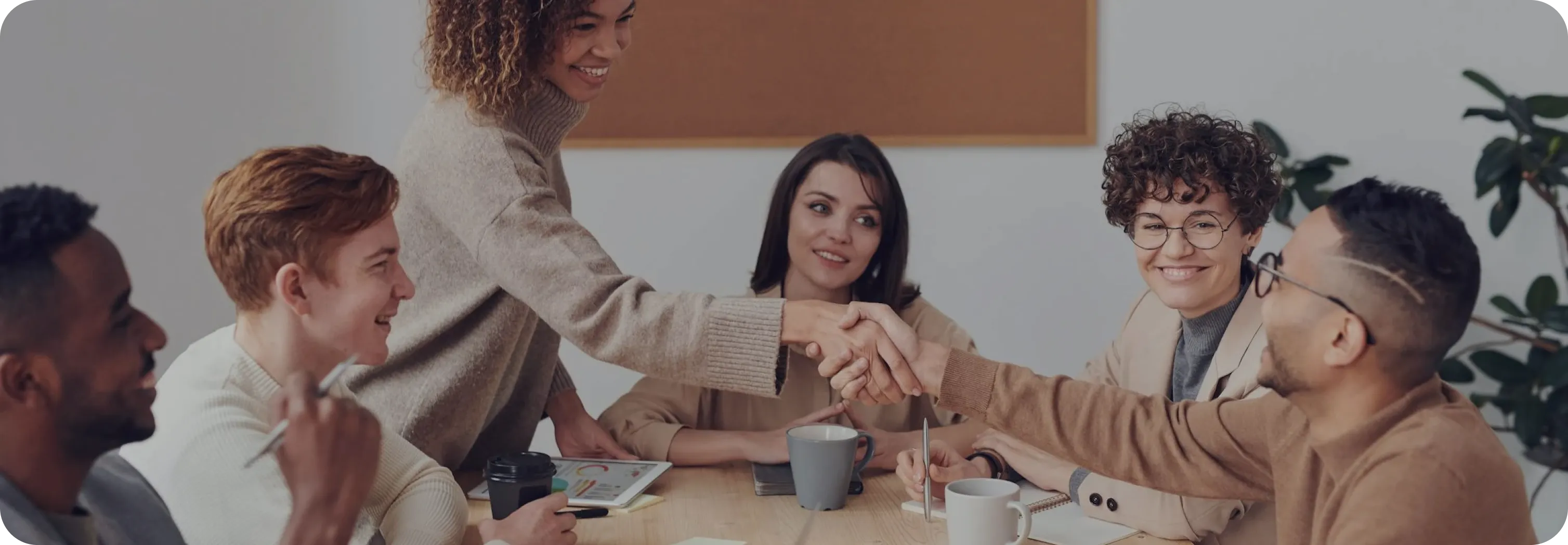 A diverse group of individuals shaking hands around a conference table, symbolizing collaboration and agreement.