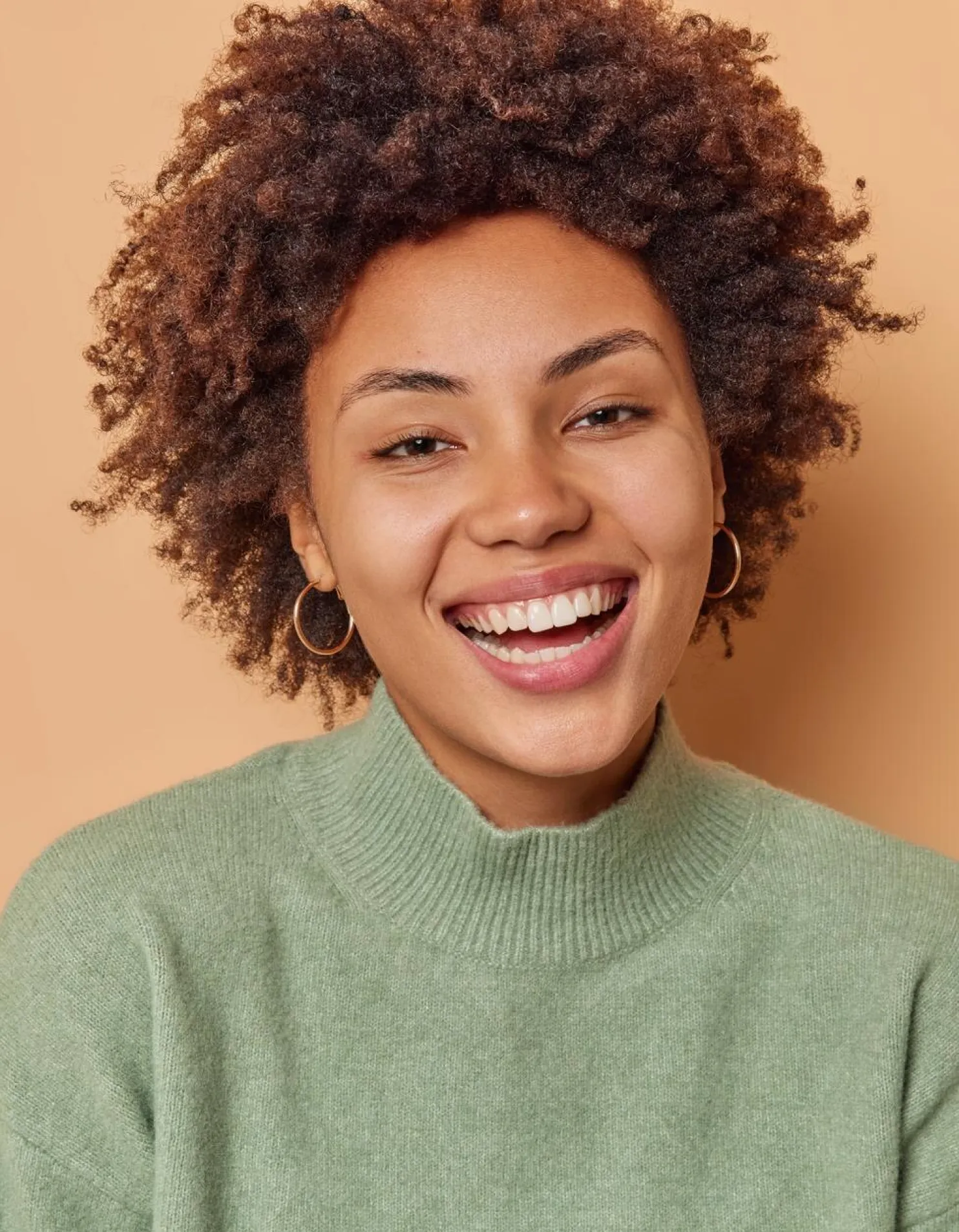 A smiling woman with curly hair, radiating joy and positivity in a bright and cheerful setting.