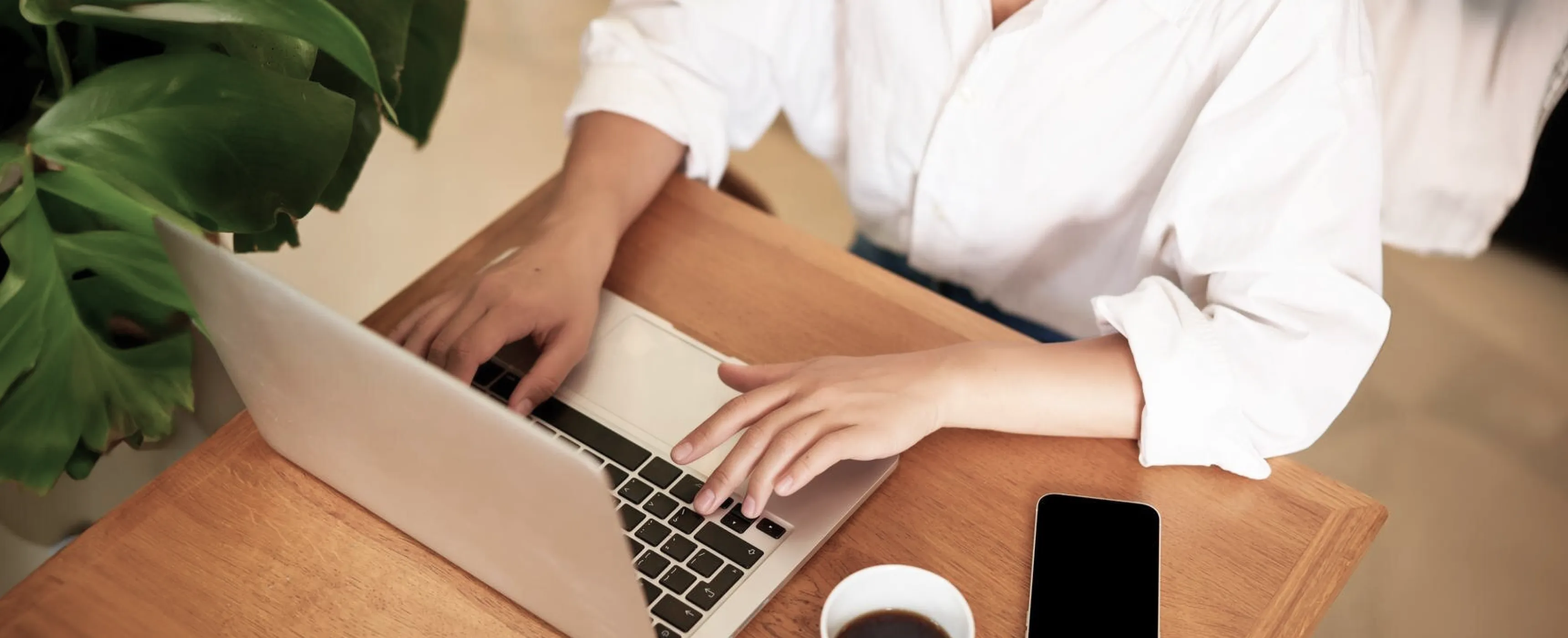 A woman focused on her laptop, typing intently at a table in a well-lit environment.