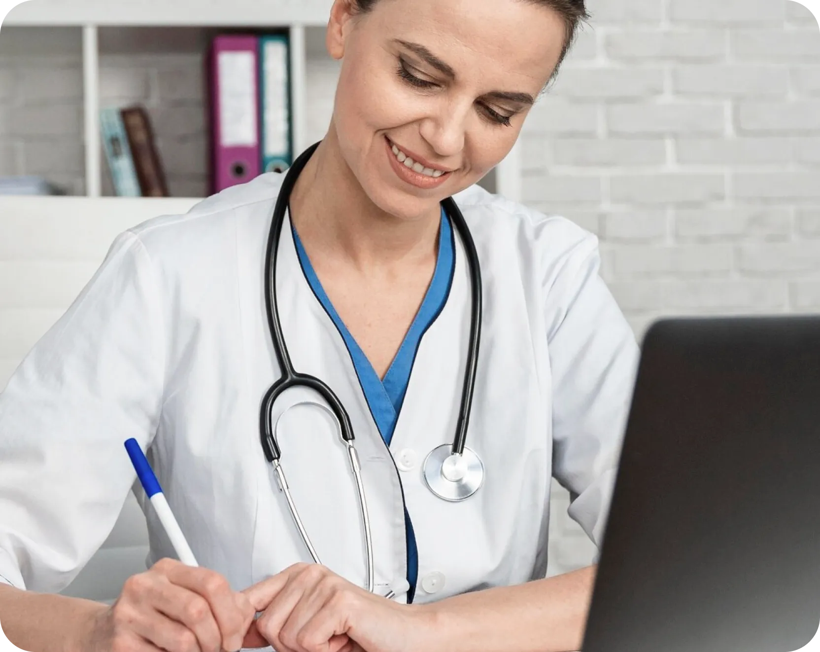 A woman in a white coat is focused on writing notes on a piece of paper at a desk.